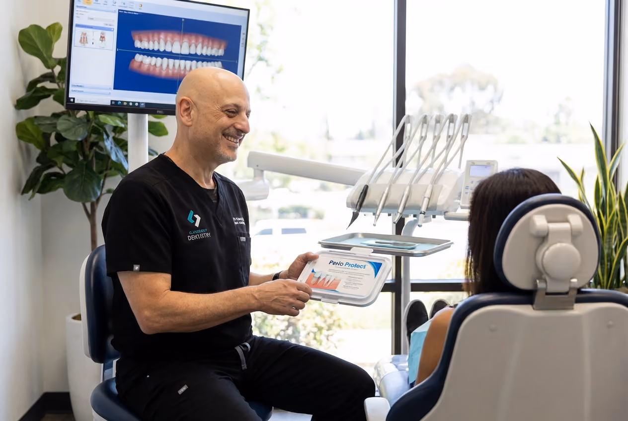A Clairemont Dentistry dentist smiles while reviewing gum health information with a patient in a dental exam room, with a digital smile image displayed on the monitor behind him.