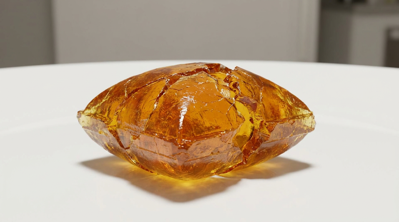 An extreme close-up on hands and object of a cracked and chipped piece of a hard candy with jagged edges, resting on a clean white surface, illustrating the potential damage to veneers.