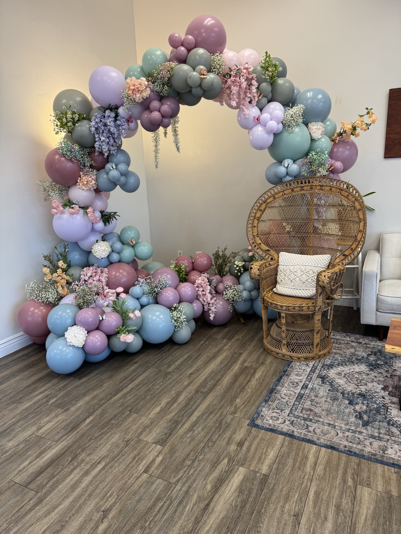 Soft floral balloon ring arch with pastel balloons and a wicker chair for a bridal shower photo area.