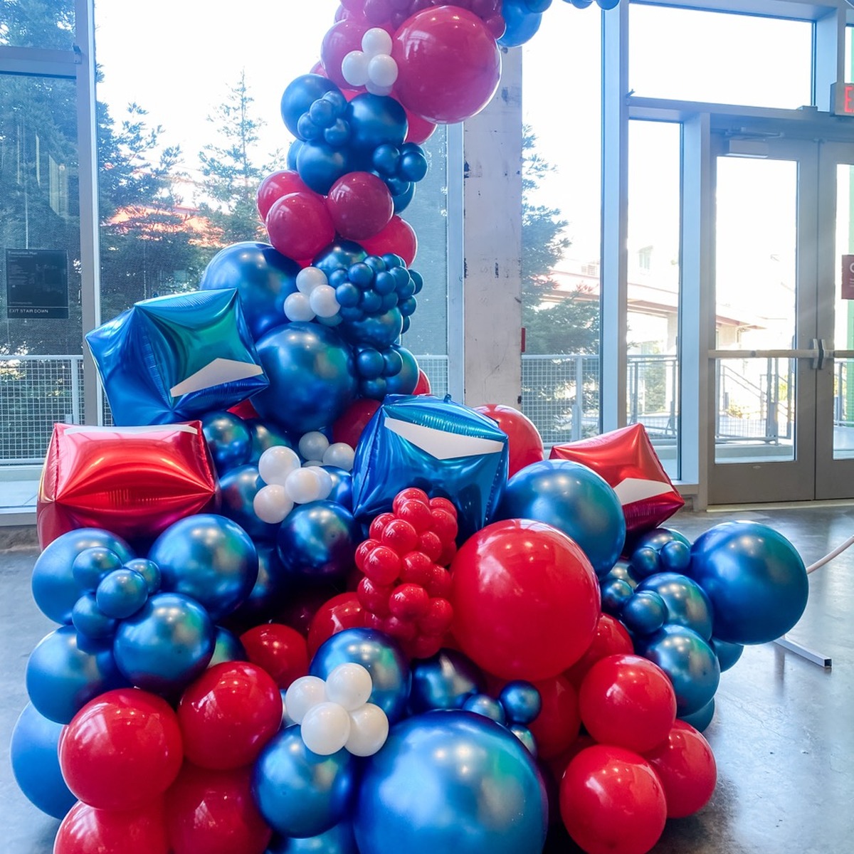 Red, blue, and white corporate balloon installation beside large windows.