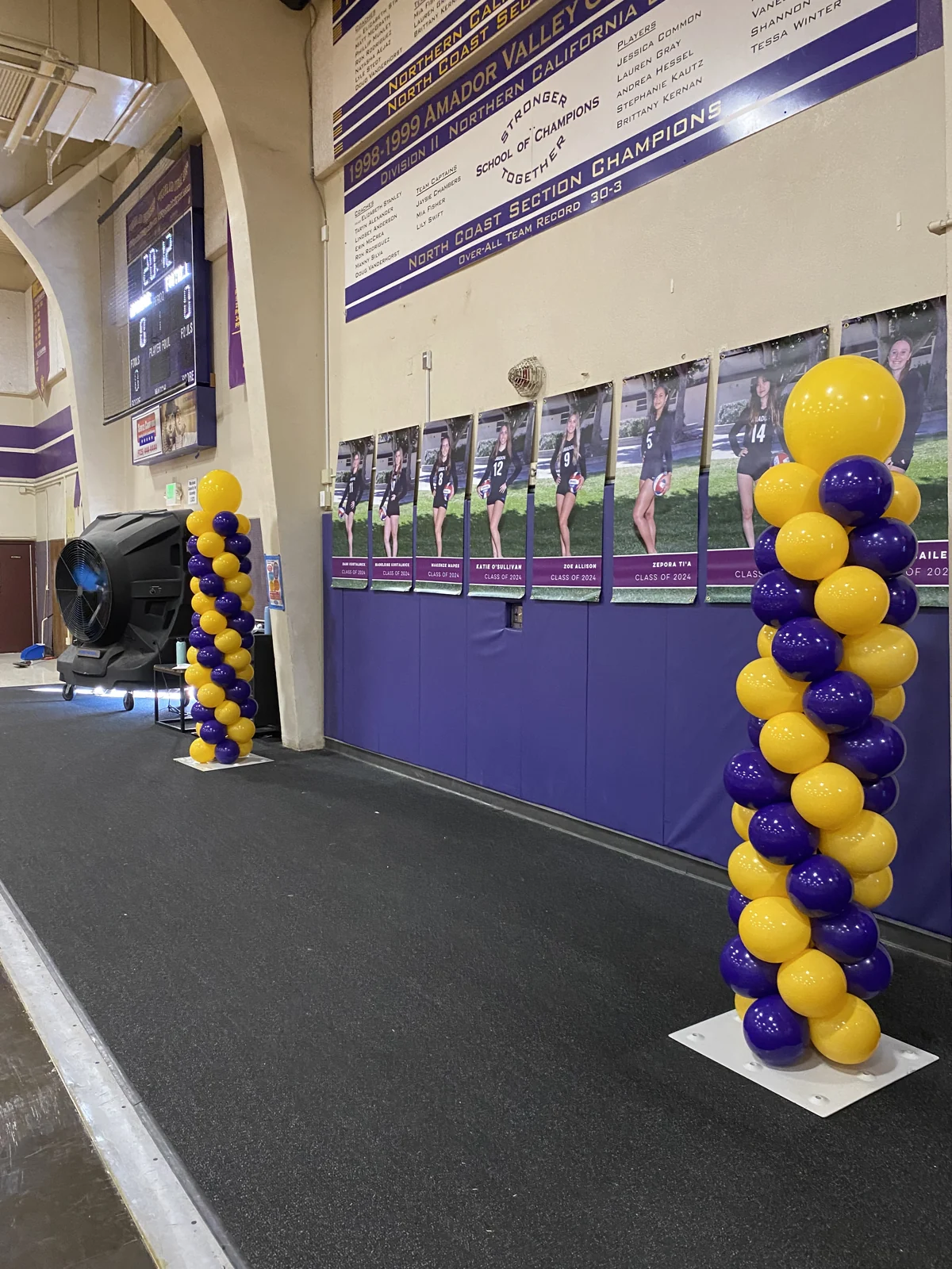 Purple and yellow spiral balloon columns along a school gym stage