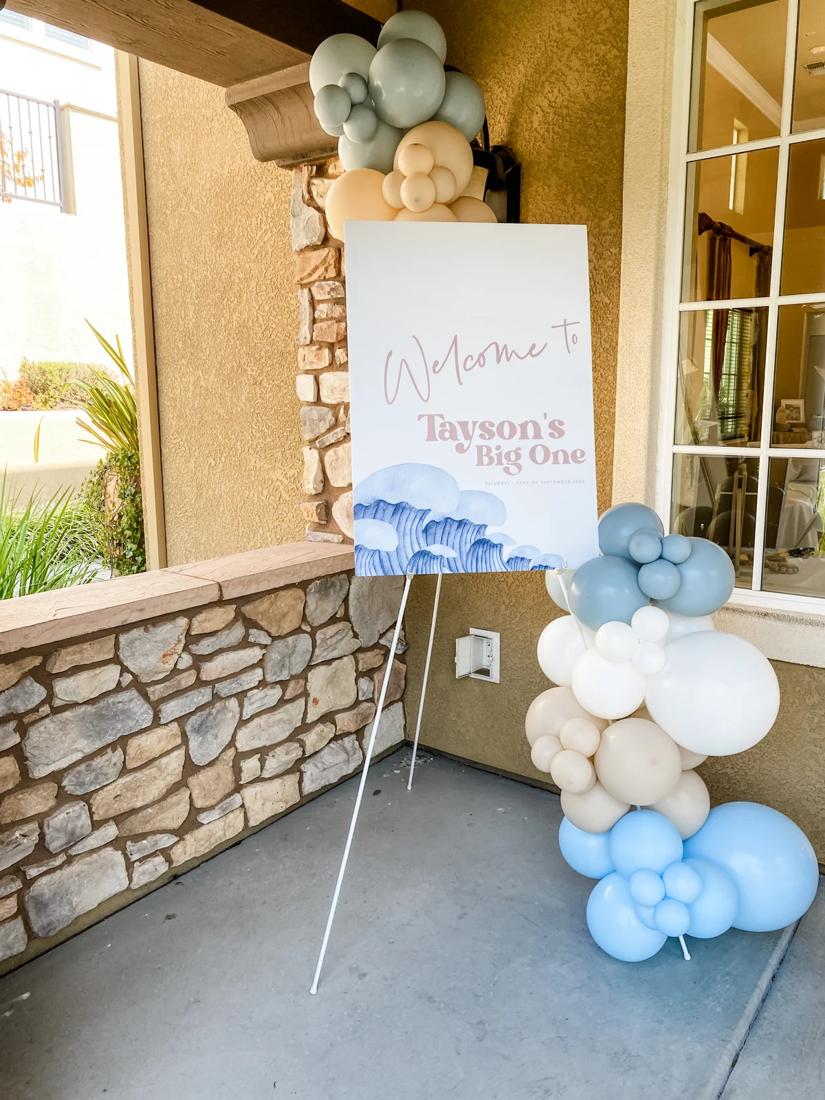 Light blue and white balloon column beside a first birthday welcome sign
