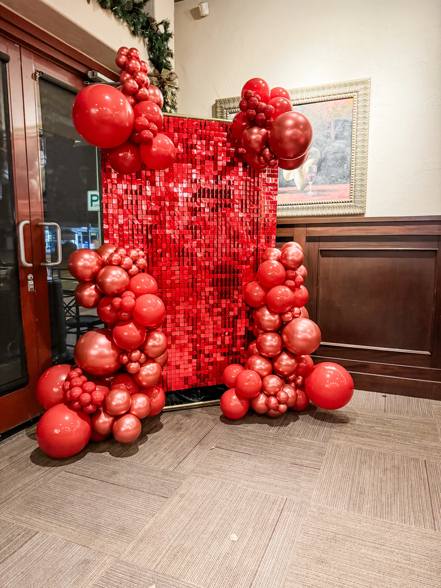 Red balloon clusters framing a red shimmer backdrop at an indoor event
