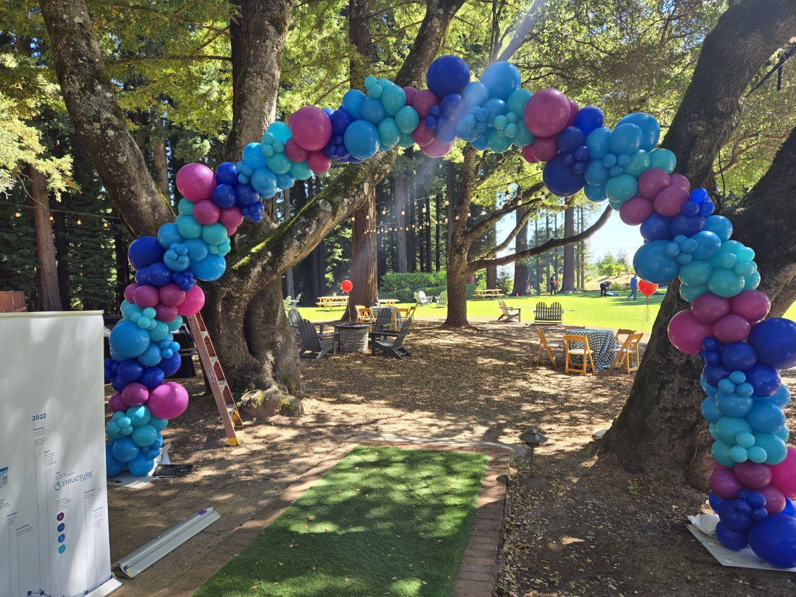 Blue, teal and purple balloon arch over a woodland event walkway