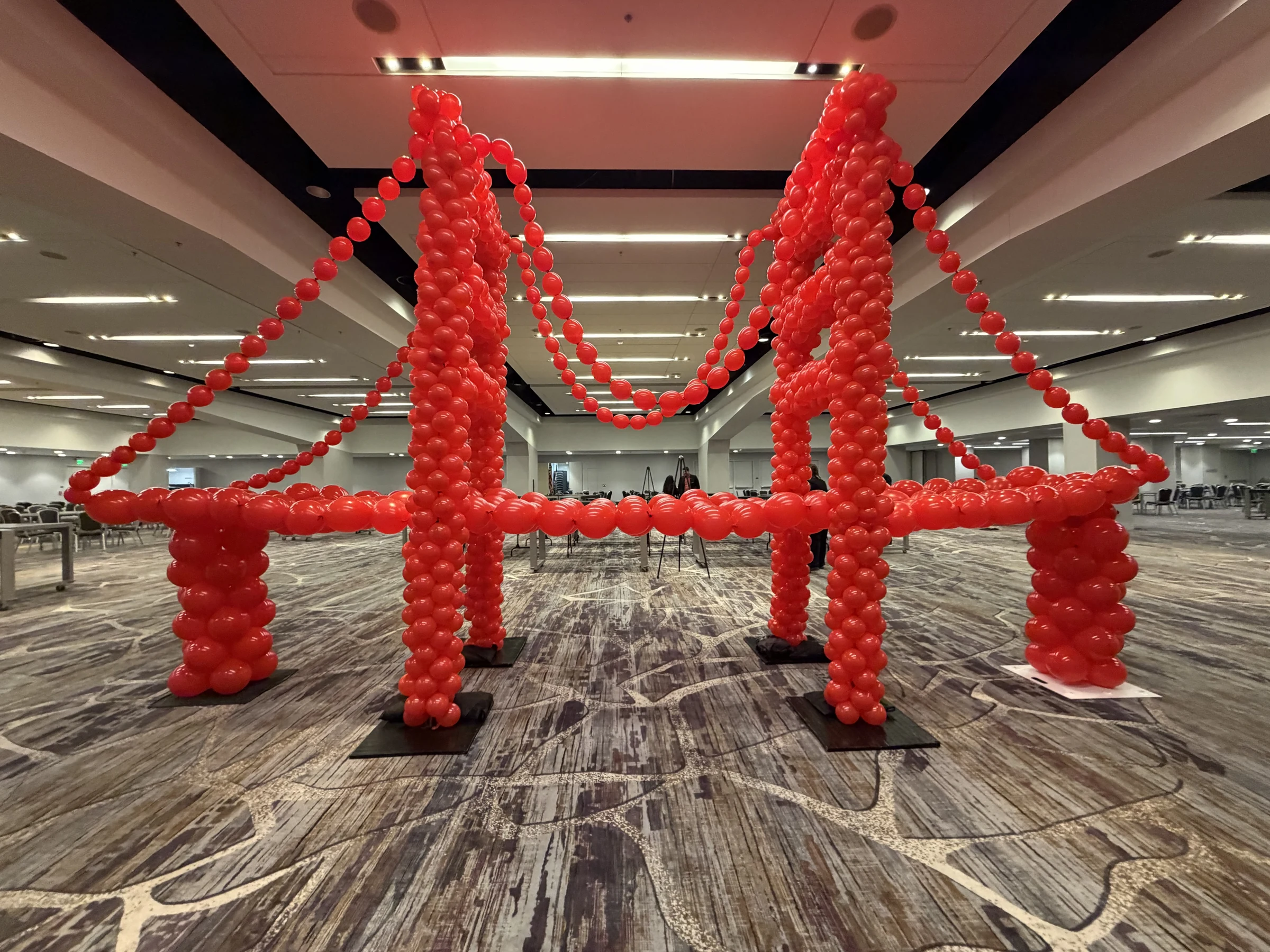 Complete red Golden Gate Bridge balloon sculpture with two towers and sweeping cable lines in a San Francisco event room
