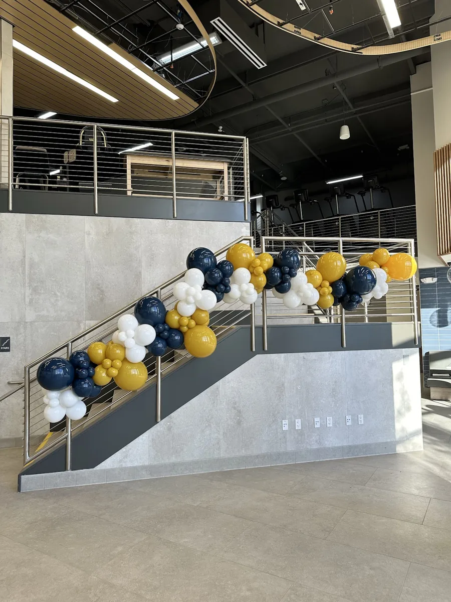 Navy, gold, and white balloon garland following the entire staircase at a company grand opening.