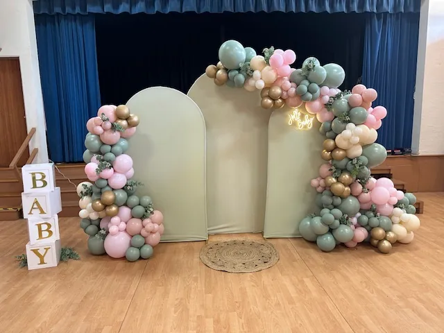 Pastel pink, sage, and gold balloon installation around cream arch backdrops, with BABY blocks.