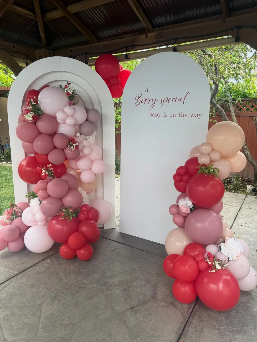 Red, pink, and cream balloons with strawberry details around a berry special baby shower backdrop.