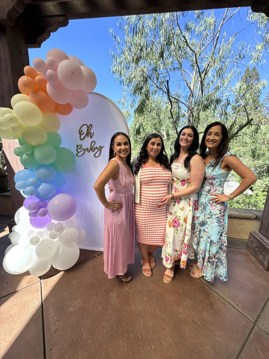Guests posing beside a rainbow pastel balloon garland and Oh Baby backdrop.