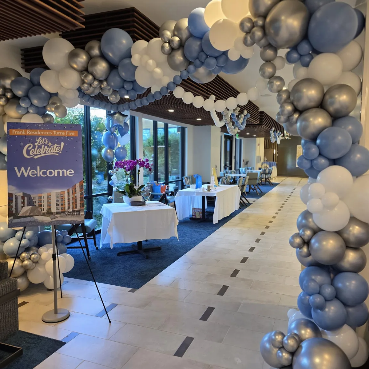 Blue, white, and silver balloon arch framing the entrance to a community celebration.