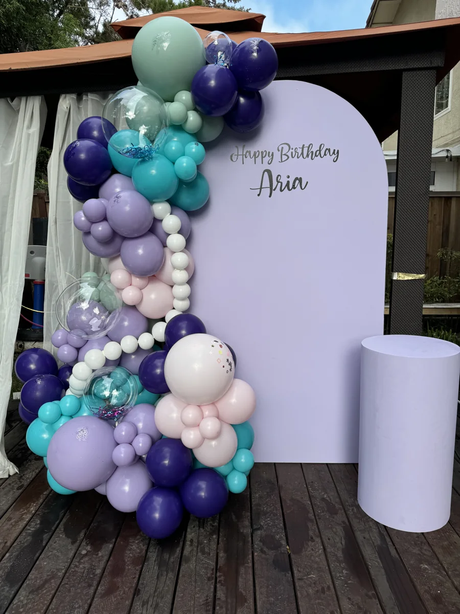 A lavender birthday backdrop with purple, aqua, and pearl balloons for a mermaid-themed fifth birthday.
