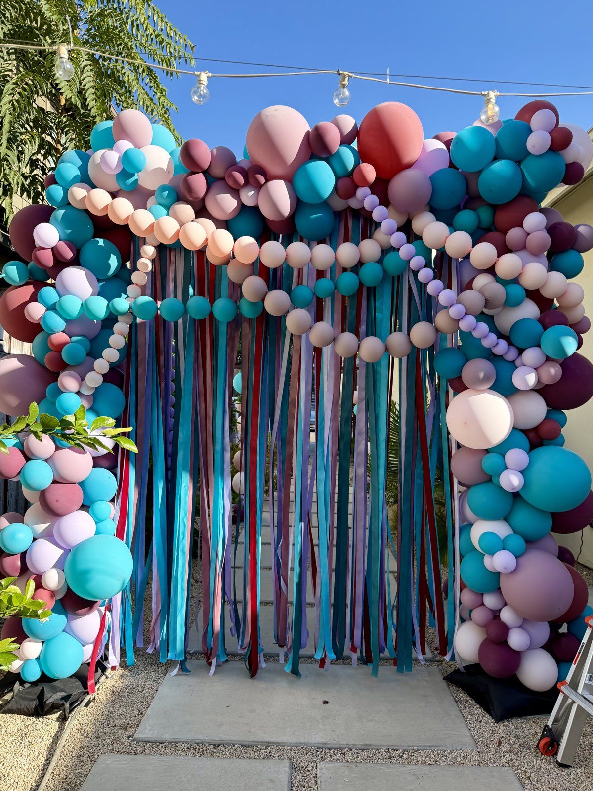 Finished squared balloon arch in Danville with teal, mauve, blush, lavender and burgundy balloon garlands and a ribbon curtain over a garden path