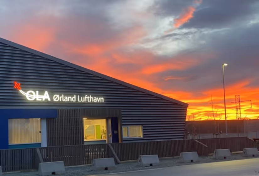 Bygning med skiltet Ørland Lufthavn opplyst ved solnedgang med oransje og lilla himmel.