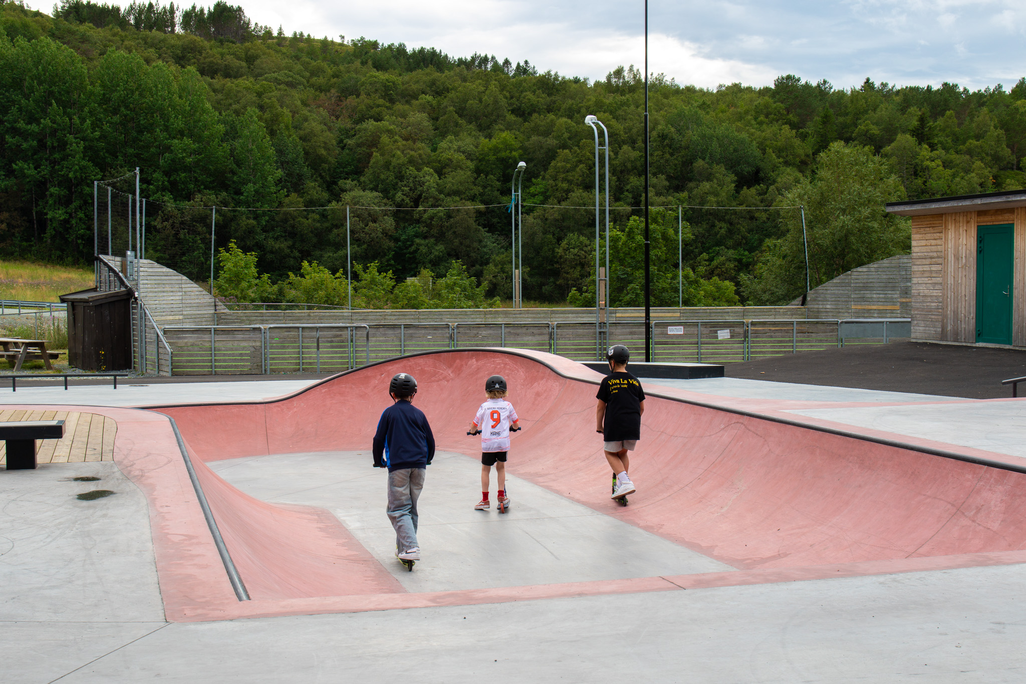Tre barn som kjører på sparkesykkel i skateanlegget.