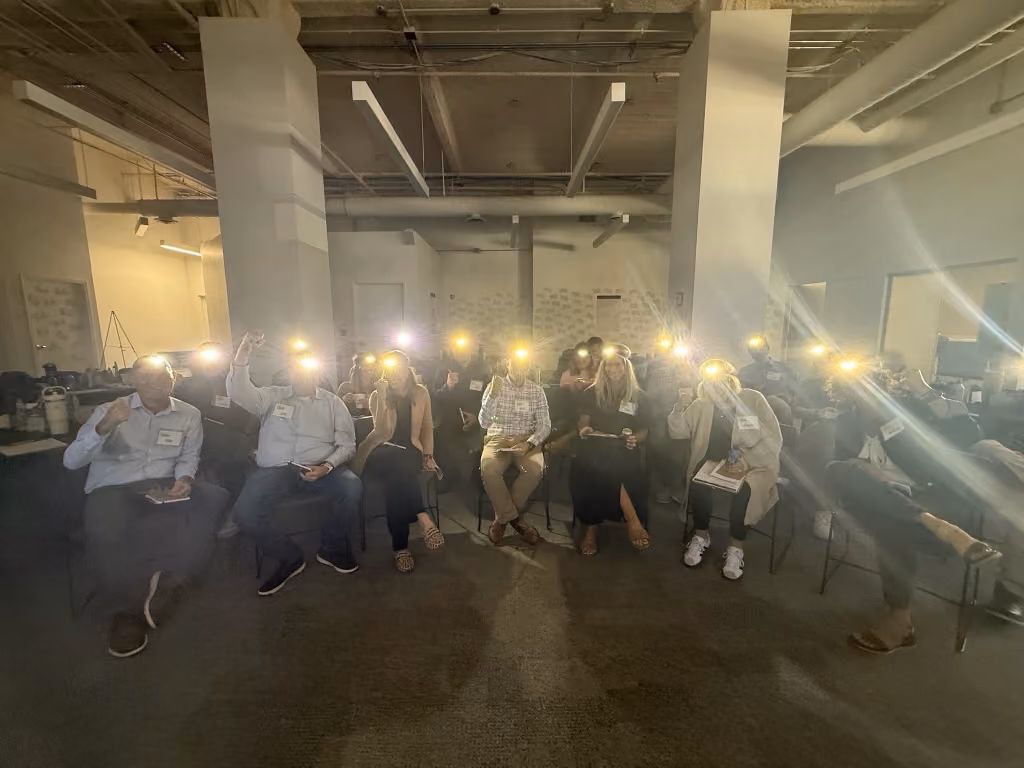 Group of people sitting indoors holding lit flashlights facing the camera in a spacious room.