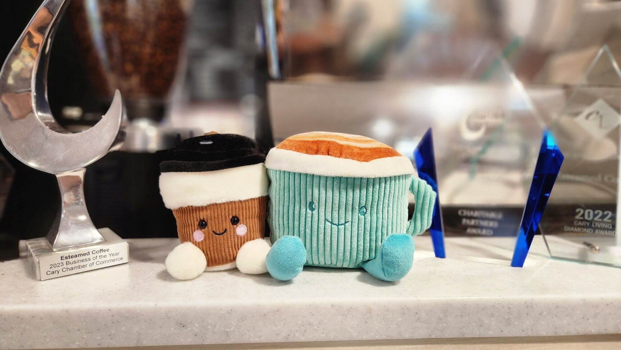 A photo of a stuffed coffee cup and stuffed coffee mug on a counter with awards.