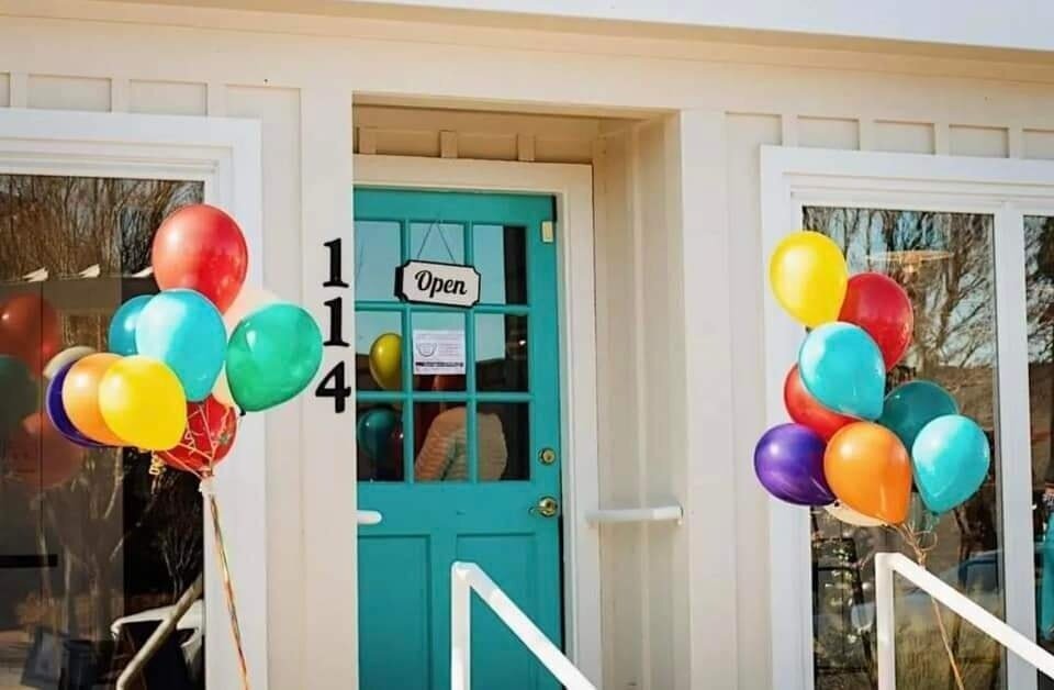 A photo of the front door of Esteamed Coffee with an "open" sign and two bunches of balloons.