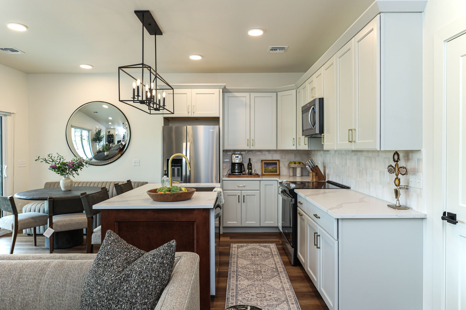 Modern kitchen with white stone countertops and crisp white cabinets. A dark brown wood center island and stainless steel refridgerator.