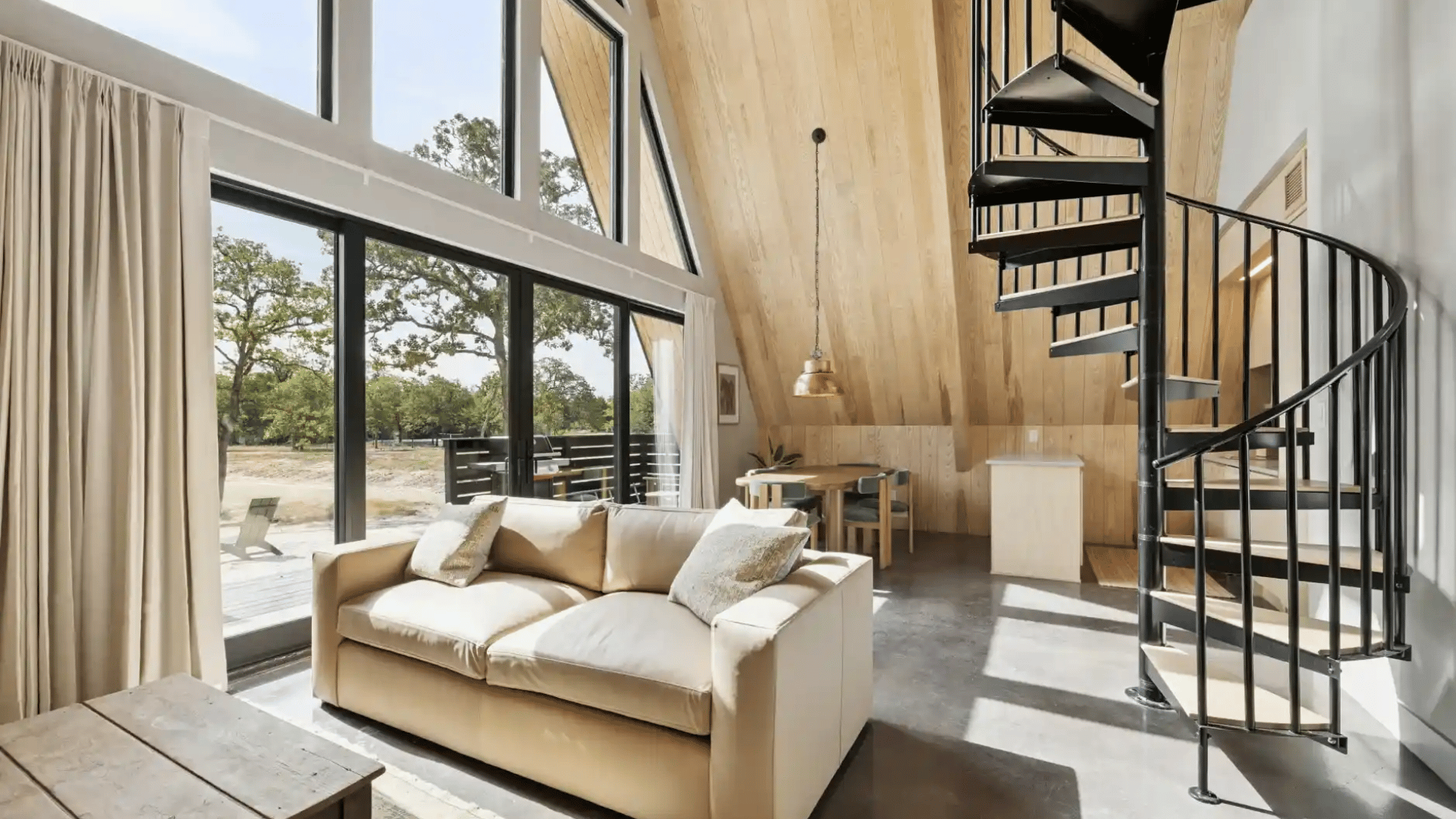 Afternoon lighting cascading through large windows into a living room with black spiral staircase in the corner.