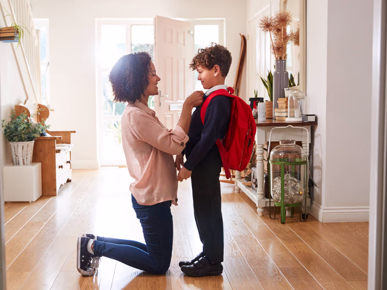 A mother on her knees as she adjusts her young son's jacket as he gets ready to leave for school