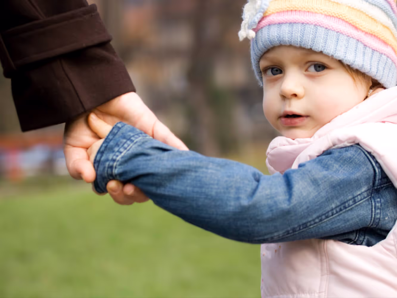 Young child wearing a winter hat and holding a woman's hand as he looks back at the camera