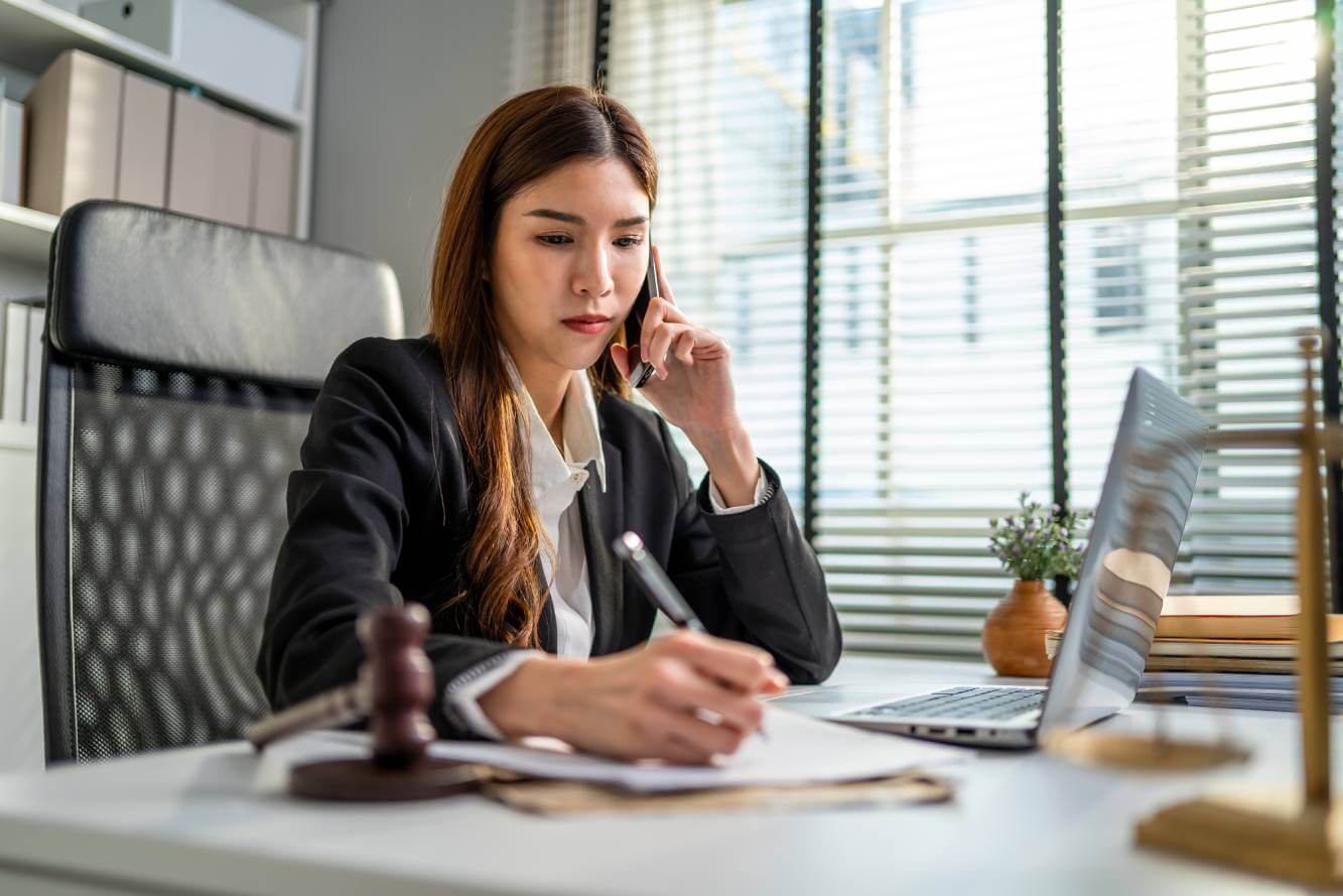 debt collection lawyer talking to small business owner on phone and taking notes as she sits at her office desk