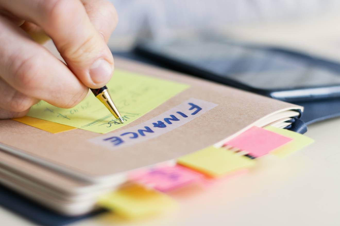 small business folder labeled finance with businessman writing on yellow note attached for folder