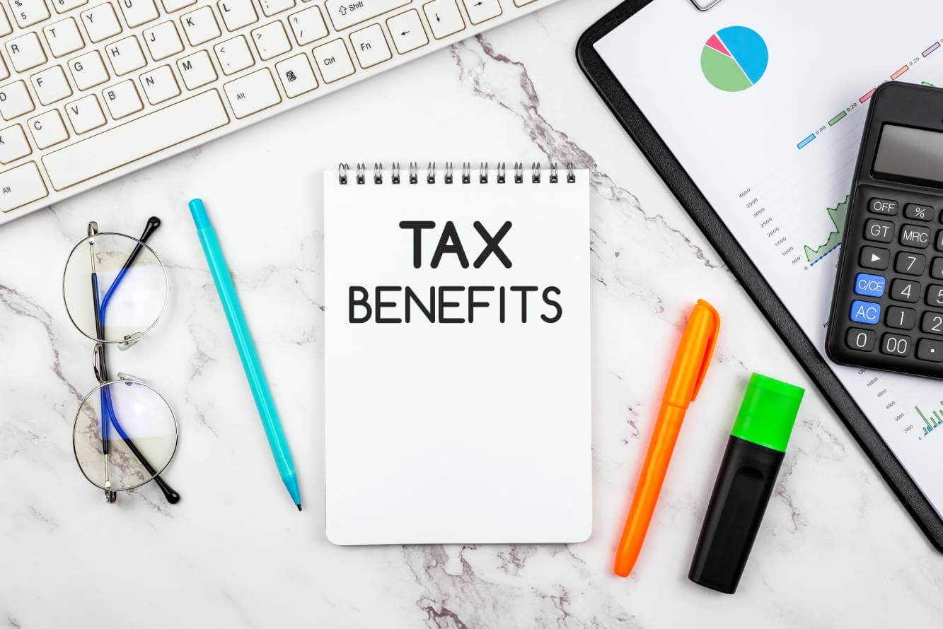 tax benefits written on a tablet on a desk next to a computer keyboard, eye glasses, writing pens, calculator and business documents