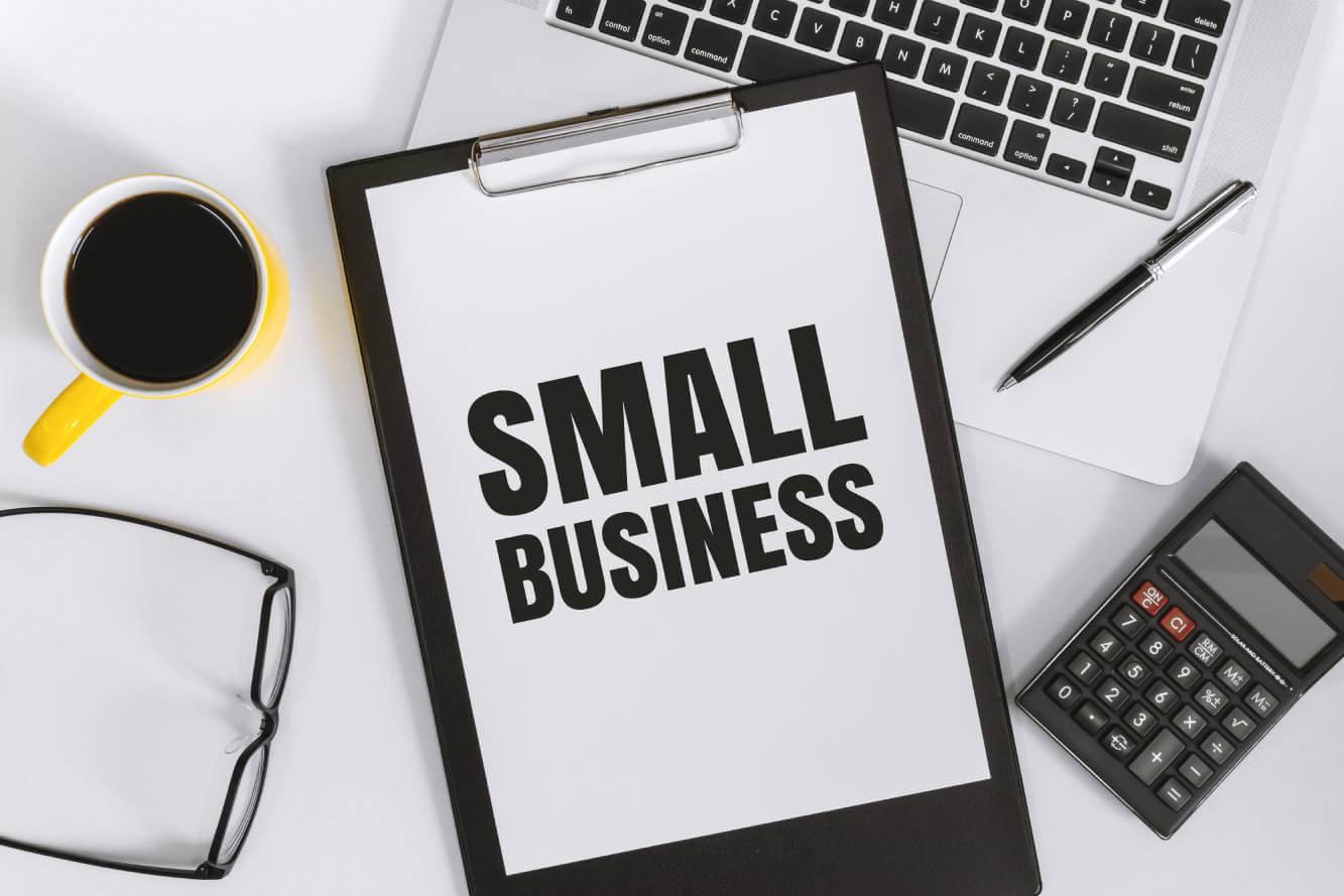 small business written on a clipboard on a desk next to coffee, eyeglasses, calculator, ink pen and keyboard