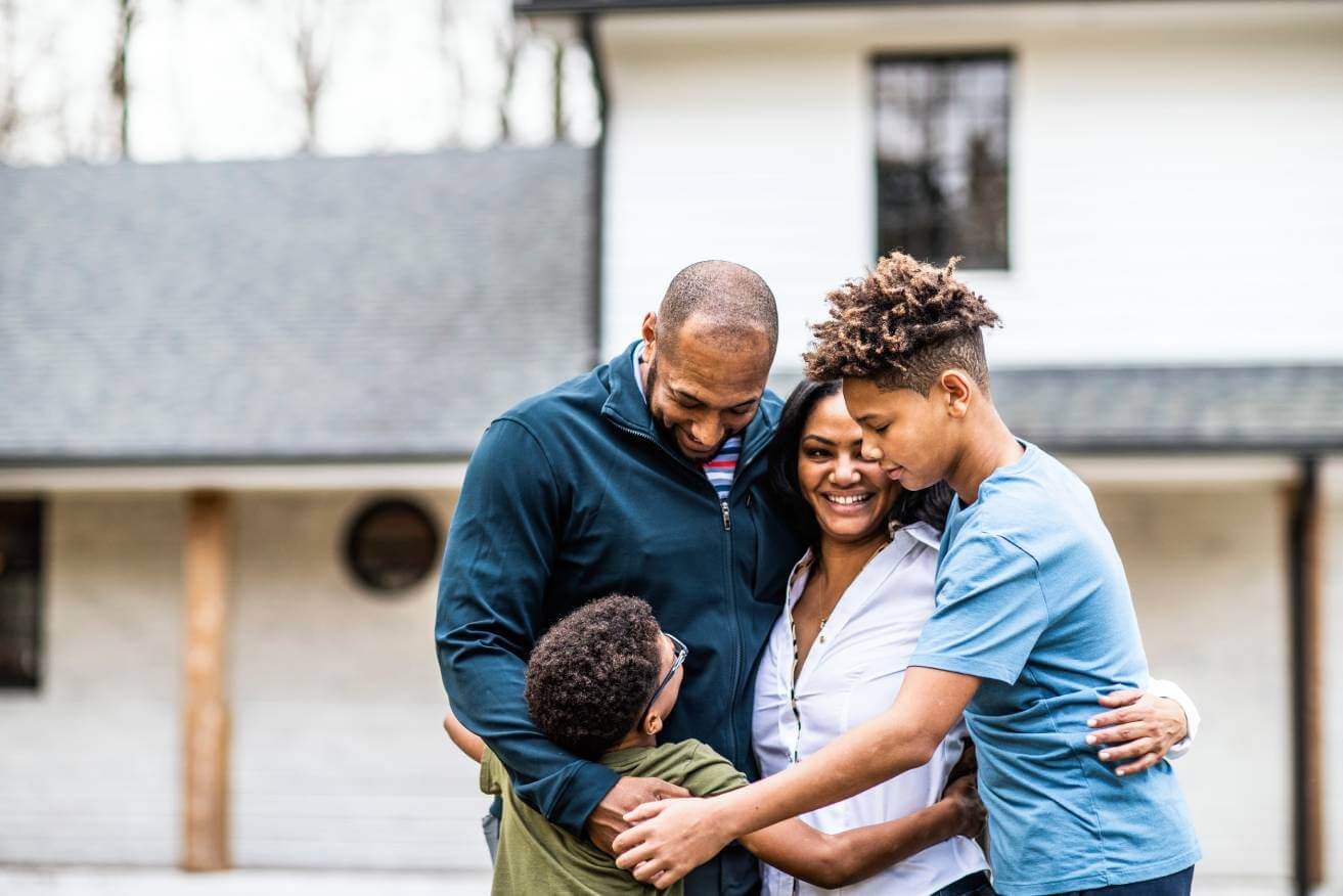 family of four embracing in yard in front of home