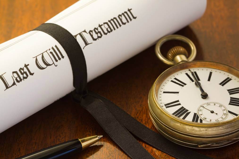 last will and testament in a scroll tied by a black ribbon next to a gold pocket watch on fountain pen