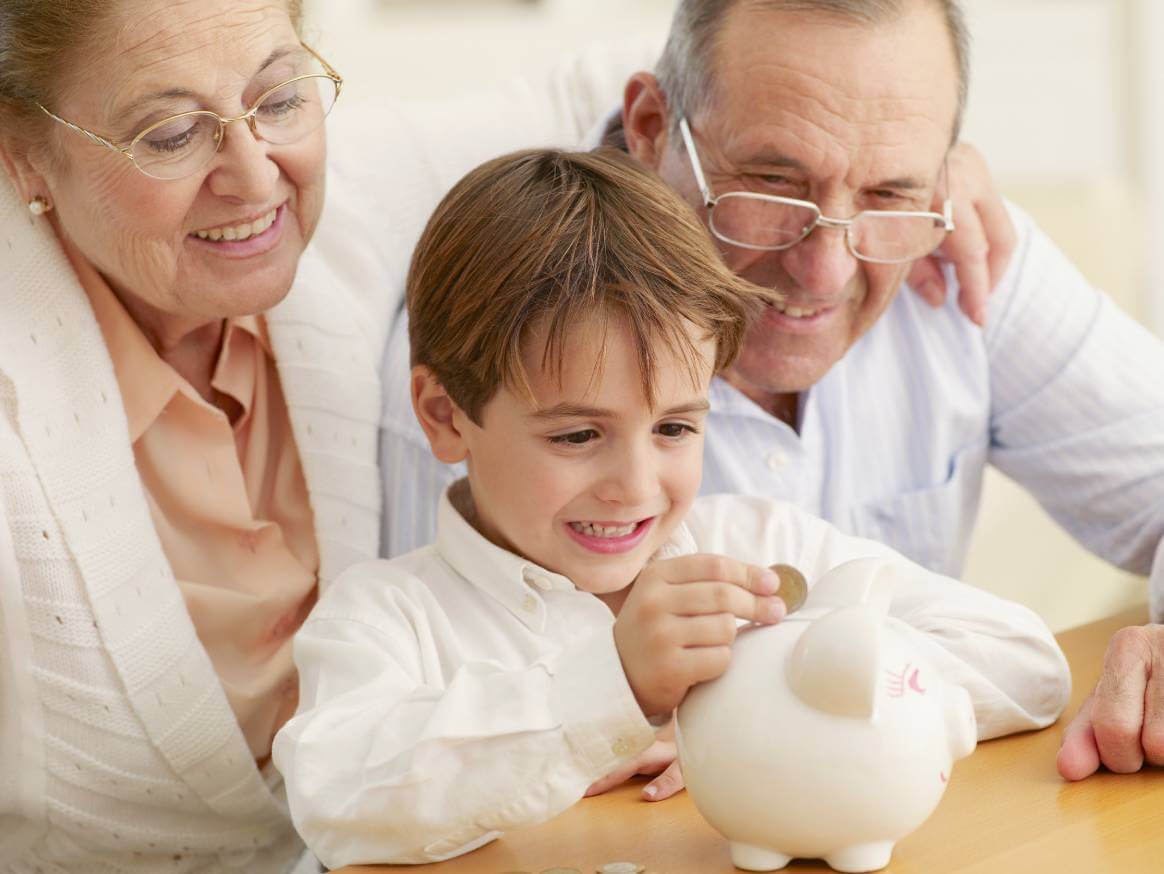 grandparents watching grandson place coins in a piggy bank