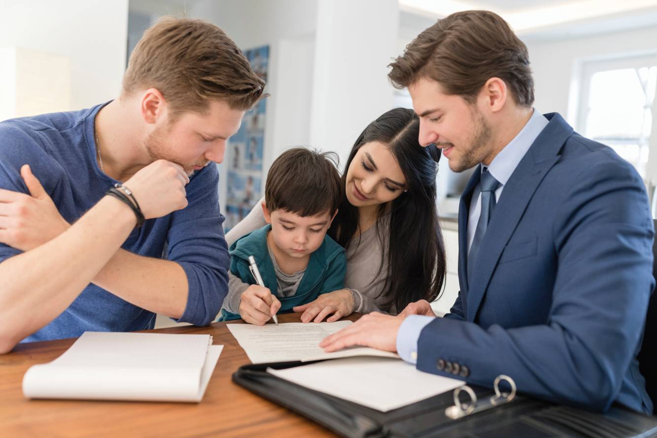 wife signing estate planning documents as lawyer and young son watch