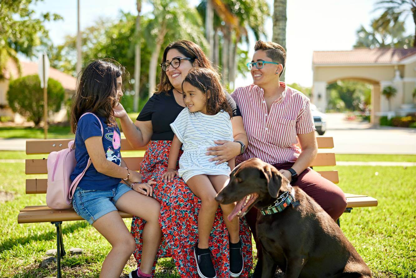 same-sex couple with 2 daughters and dog sitting on a park bench