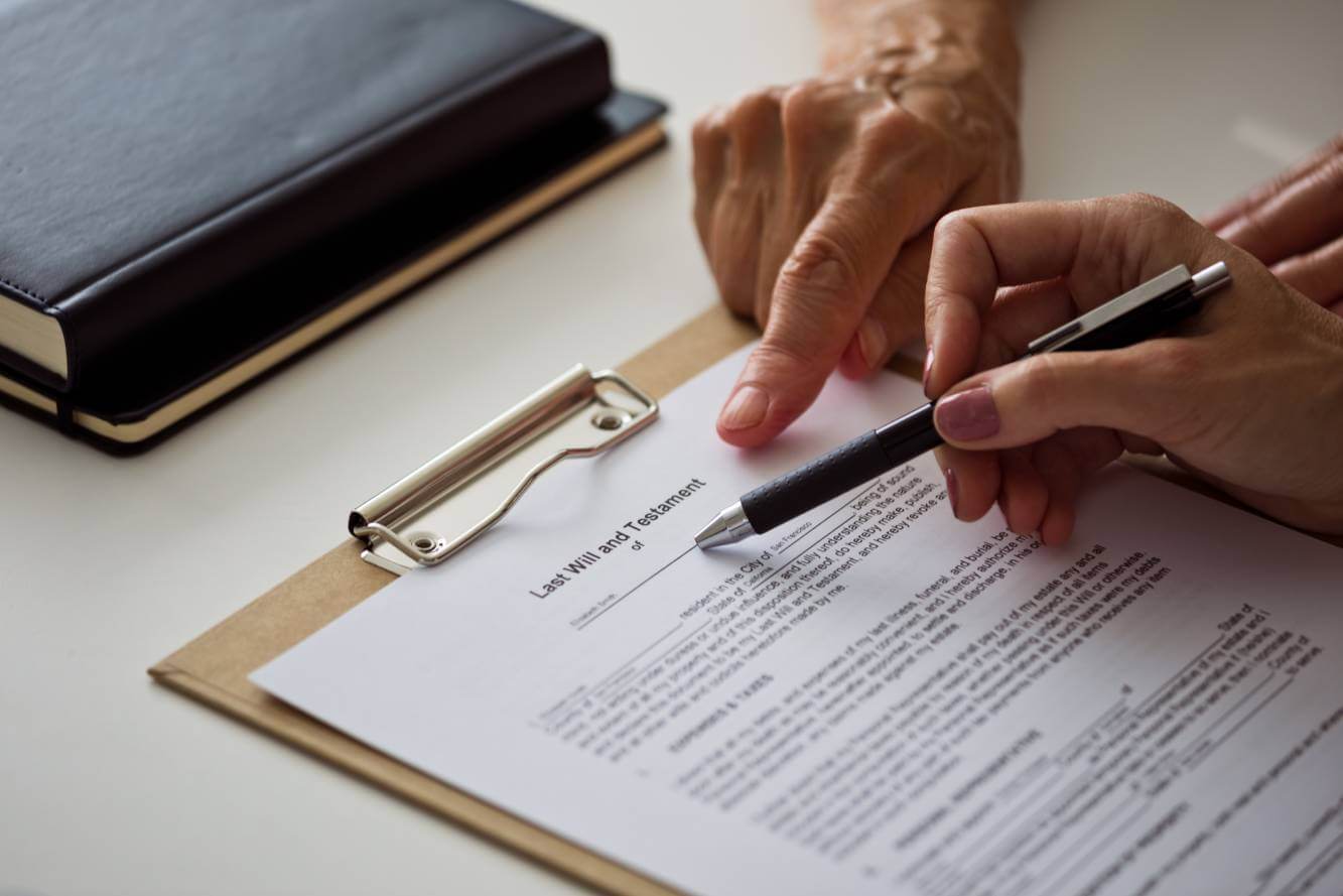 lawyer pointing to a section of a written Last Will and Testament as a client reviews for signature