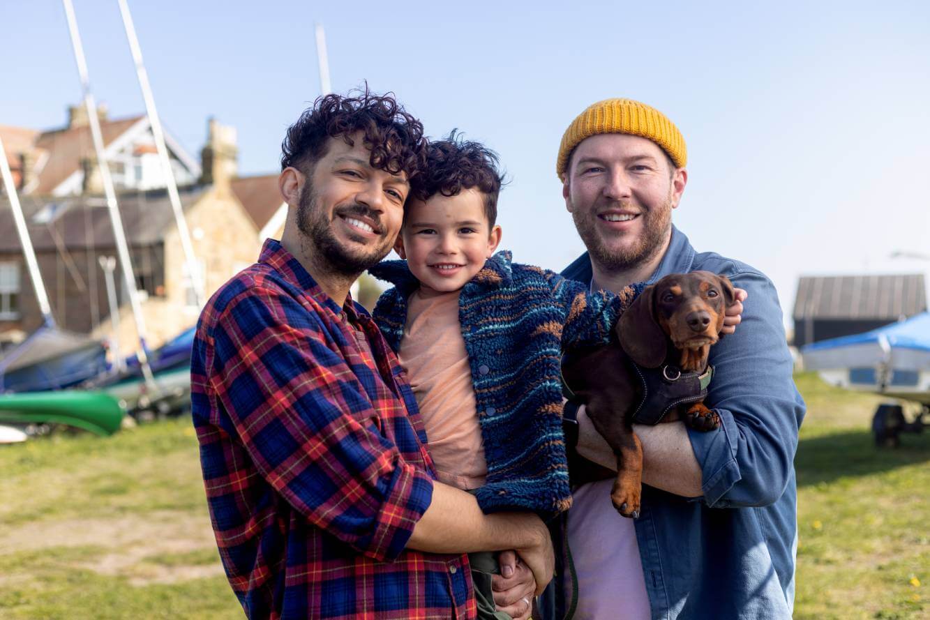 same-sex couple and their young son and dog standing outside by boats