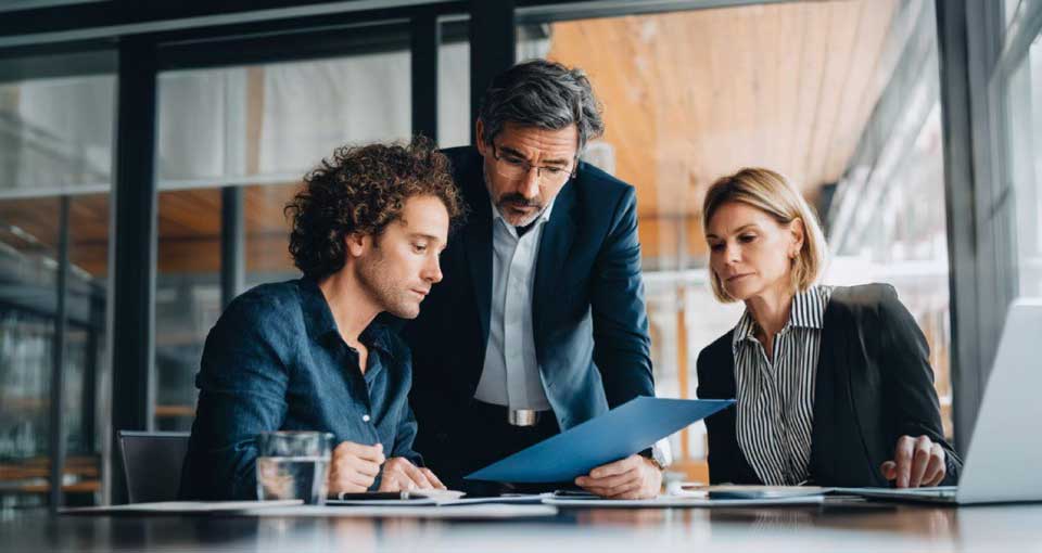 Three business professionals reviewing a document together in a modern office.