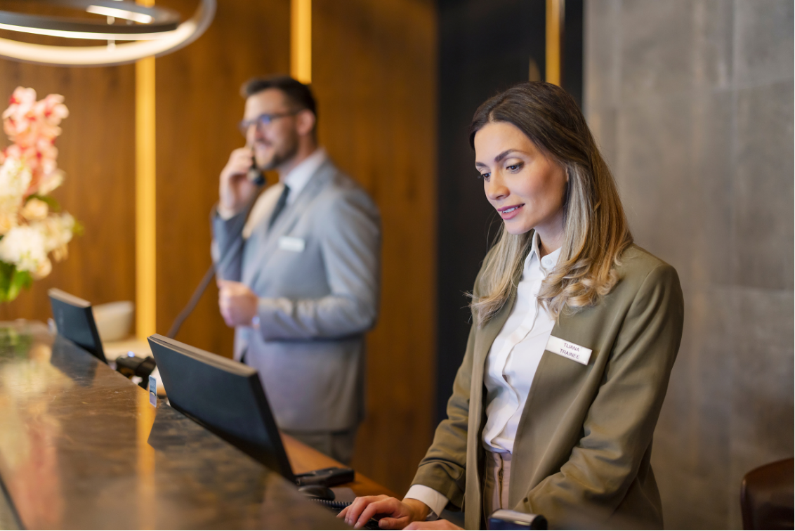 Two hotel front desk staff working at the reception counter, one on the phone and one at a computer