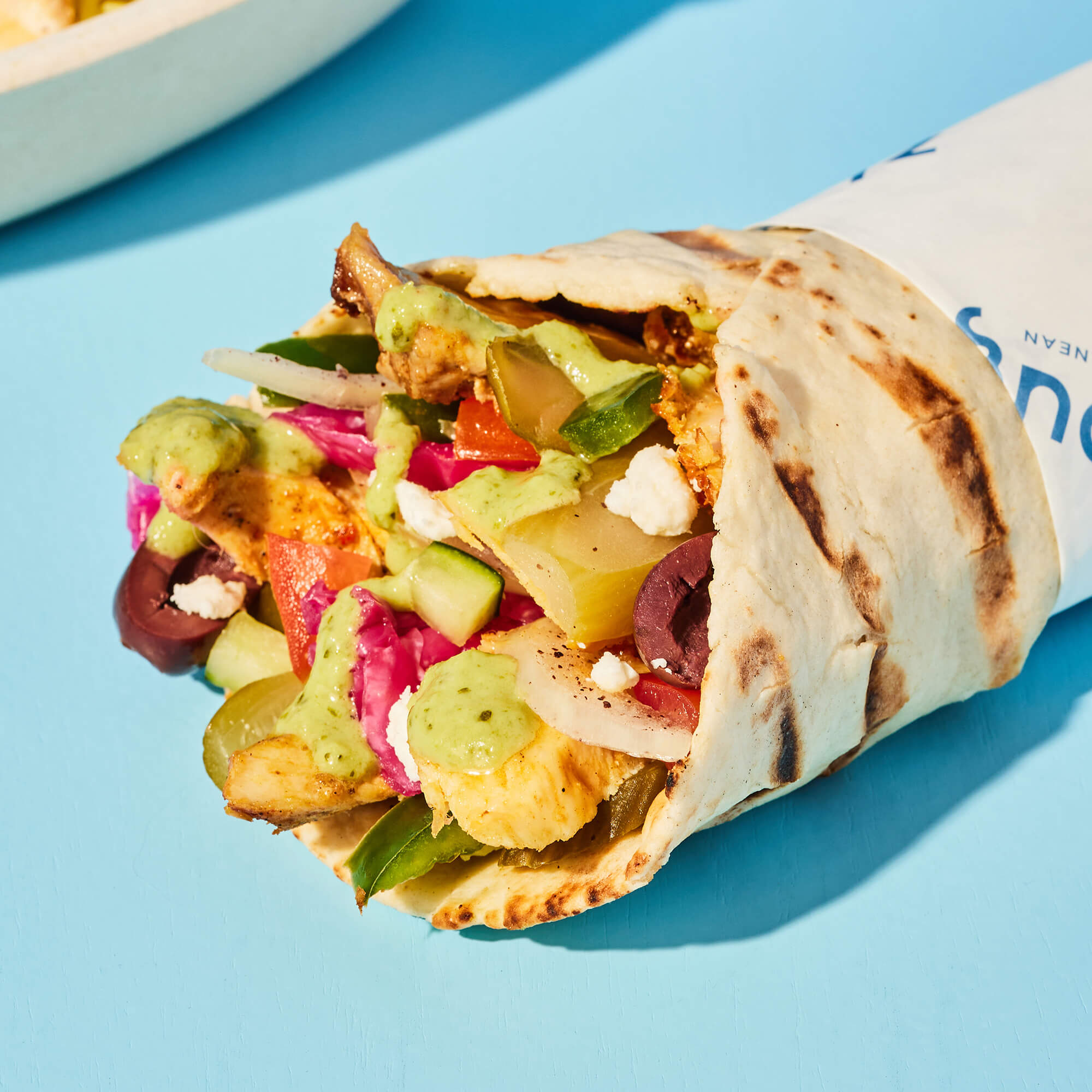Delicious chicken shawarma pita wrap on a blue surface.