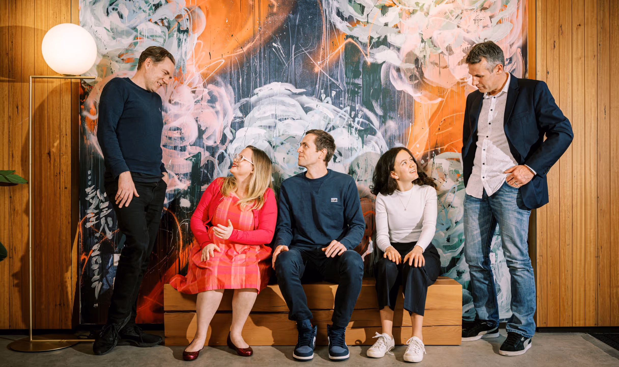 A group of people sitting on a bench in front of a painting.