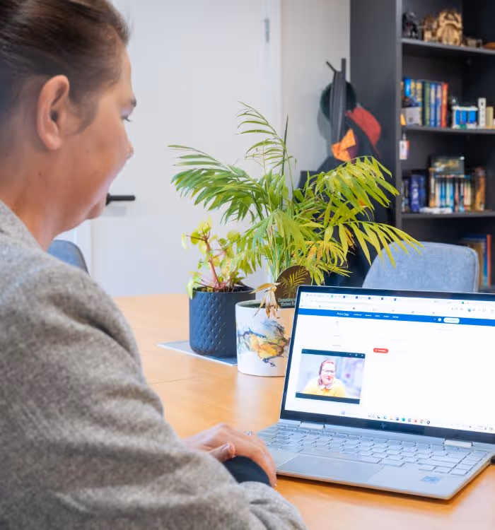 A woman is sitting at a desk with a laptop and a potted plant.