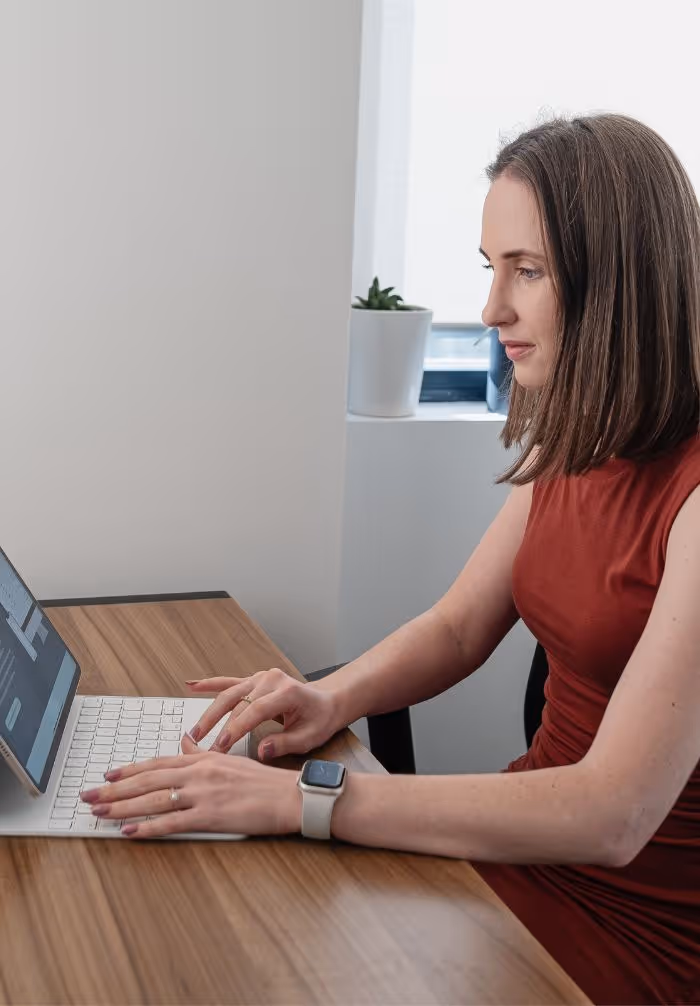 A woman in an orange shirt is typing on a laptop.