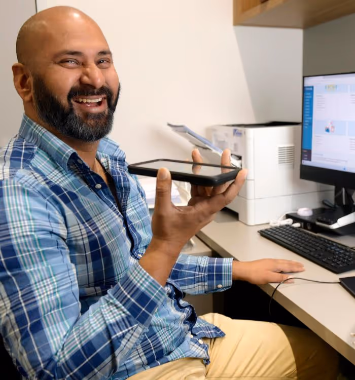 A man with a beard and a blue plaid shirt holding a cell phone.