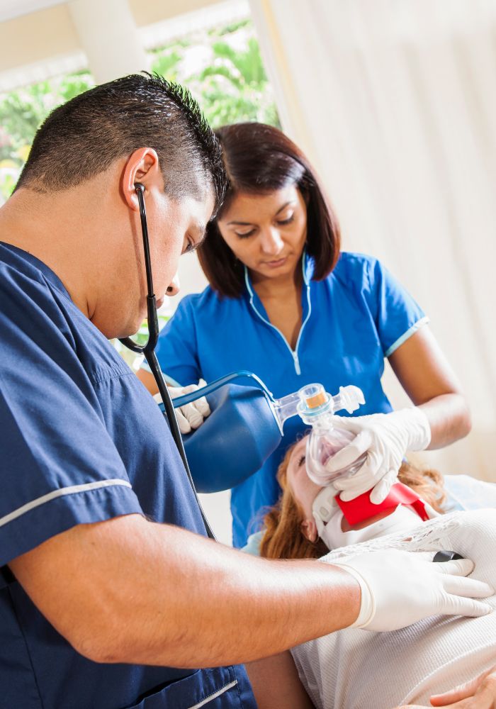 A man and woman nurse  in a blue is giving a patient oxygen.