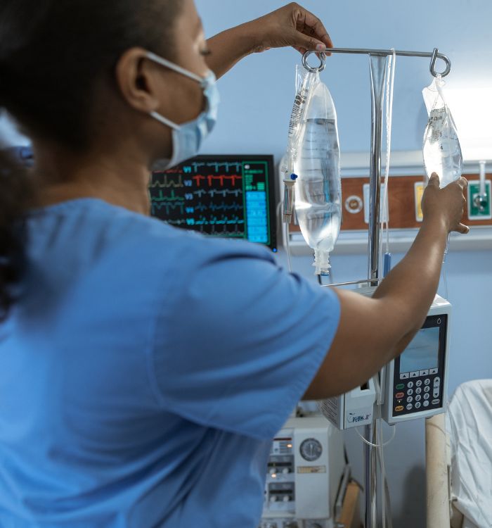 A woman in a blue scrub is adjusting a drip bag.