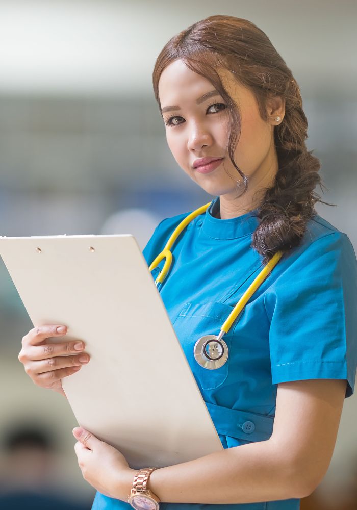 A woman in a blue scrub is holding a clipboard.