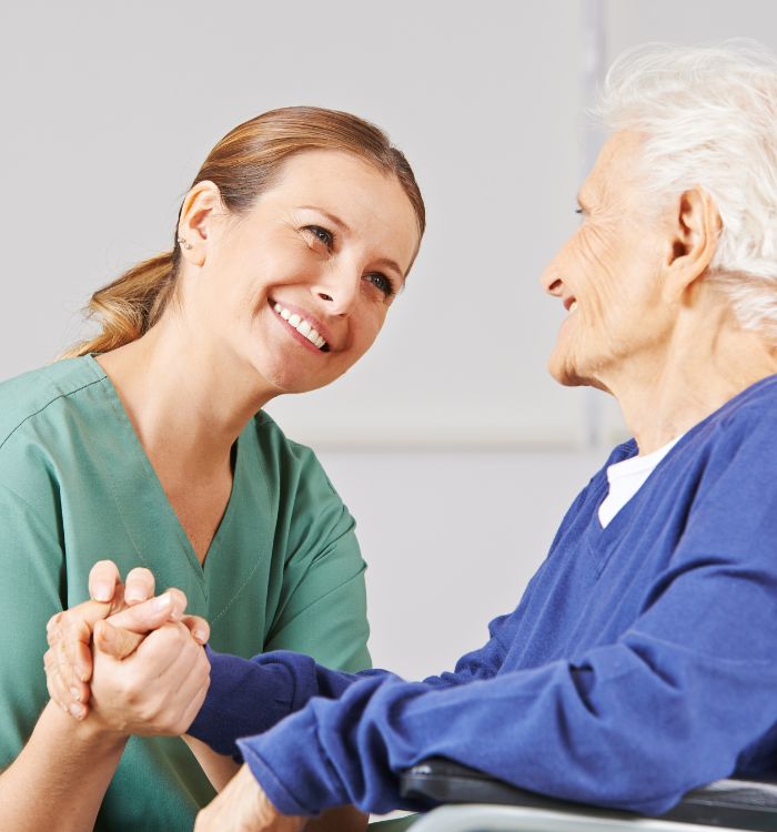 A woman in a green scrub is holding hands with an elderly woman.