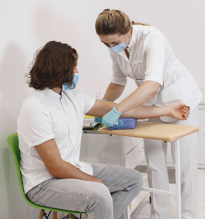 A nurse in white scrub is attending a male patient with a blue mask on his face.