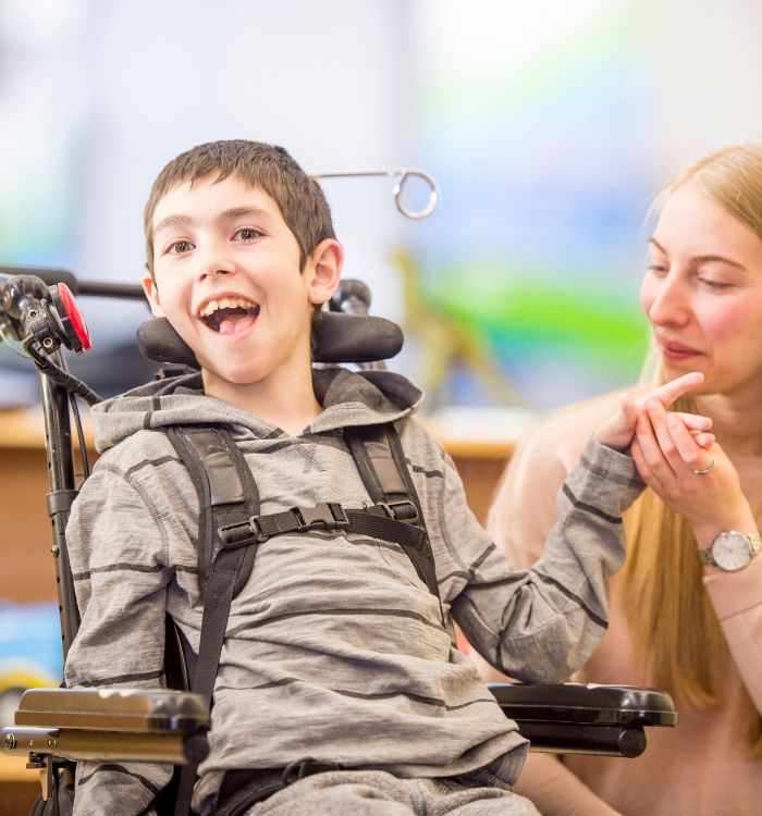 A boy in a wheelchair with a woman holding his hand.