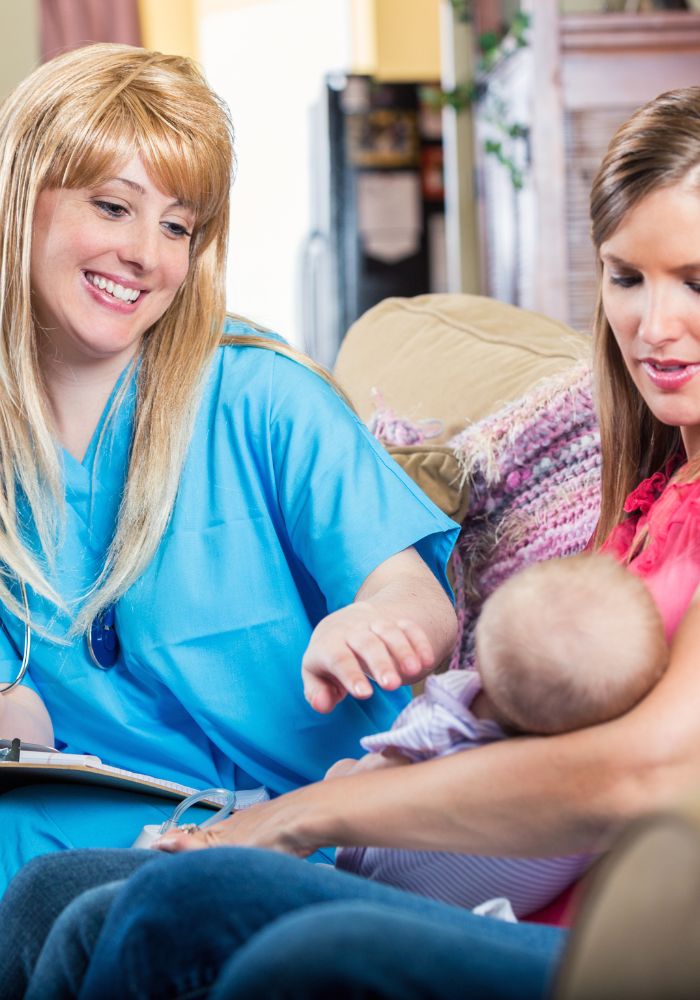 A woman in blue scrub is smiling at a baby held by a woman in pink.